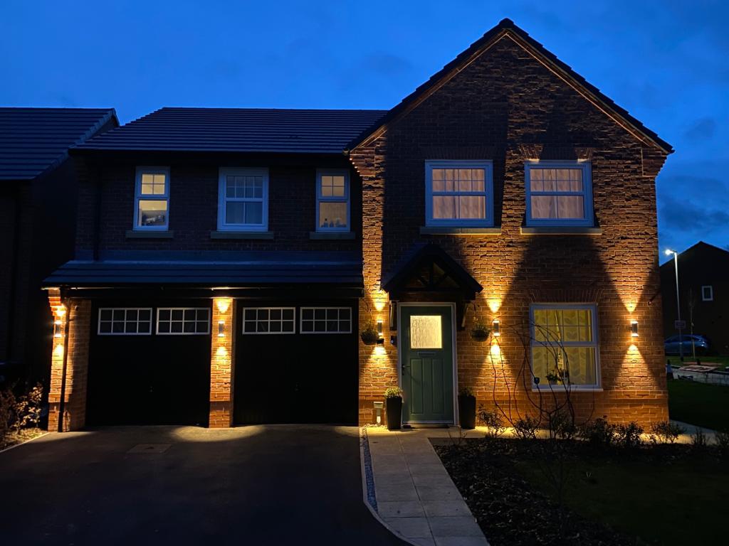 A new-build house at dusk with the external wall lights and porch lights we fitted switched on