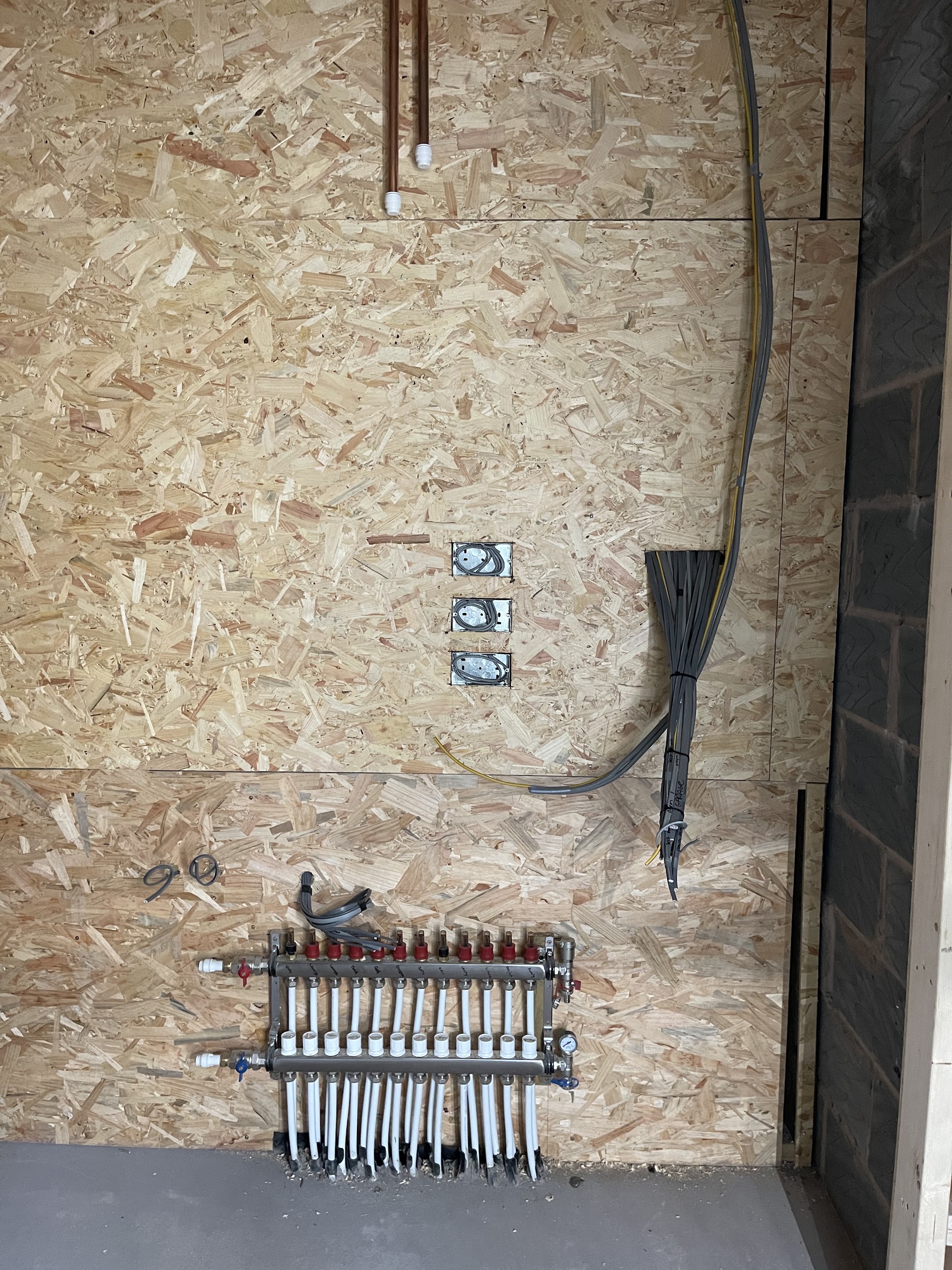 An underfloor heating manifold and controls on an OSB wall, cables ready