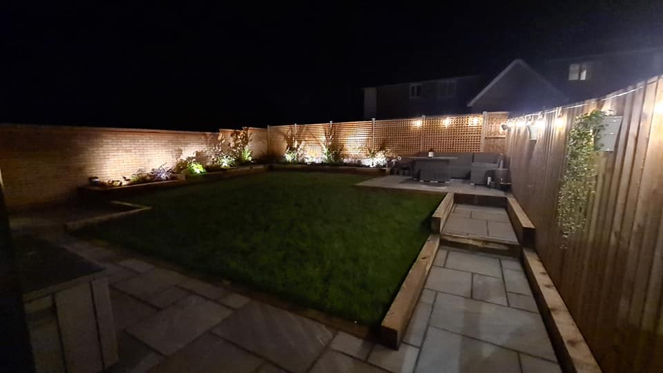 A lawn and patio at night with fence lights all along the boundary