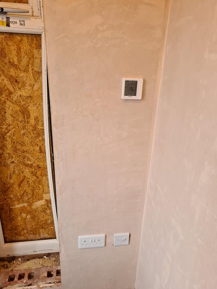 A thermostat and sockets on a freshly plastered wall