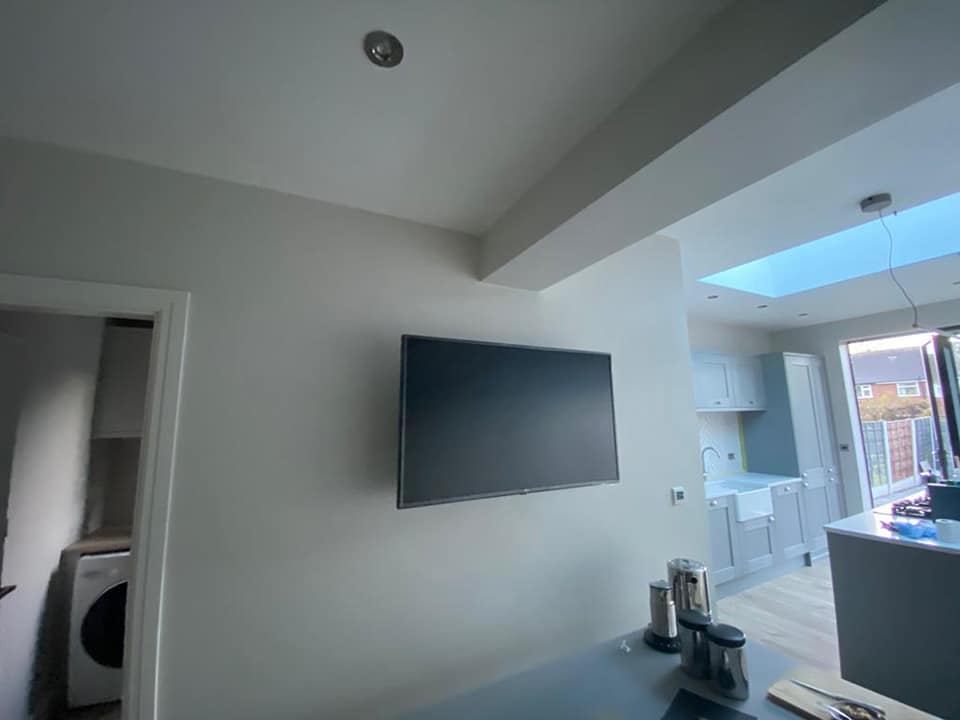 An open-plan extension with a wall-mounted TV and the kitchen beyond